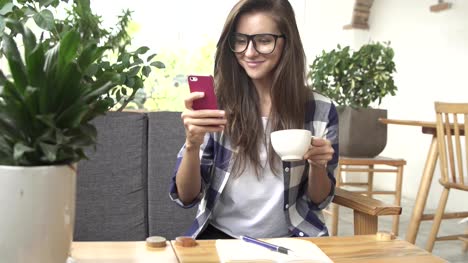 Woman-using-app-on-smartphone-in-cafe-drinking-coffee-and-laugh