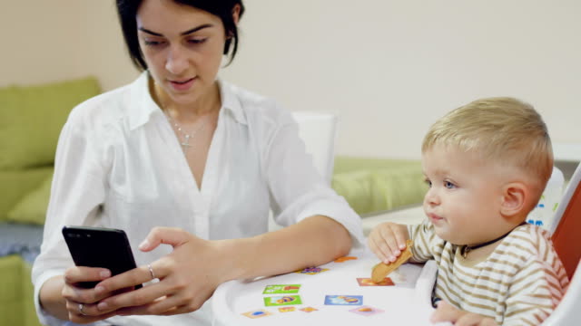 Mother-uses-phone-during-little-son-eating-biscuit