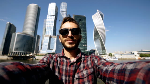 Hombre-de-turista-feliz-tener-chat-de-vídeo-en-línea-usando-su-smartphone-cámara-cerca-de-centro-internacional-de-negocios-en-Moscú