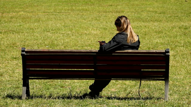 Porträt-der-jungen-Frau-mit-Smartphone-sitzen-auf-einer-Bank-im-park