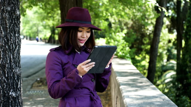 smiling-sophisticated-chinese-woman-using-tablet-in-the-street,portrait
