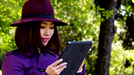 Hermosa-mujer-asiática-utilizando-la-computadora-de-la-pc-de-la-tableta-en-un-parque