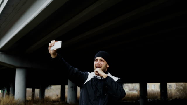 Hombre-deportista-feliz-tomando-selfie-retrato-con-smartphone-después-de-entrenamiento-de-boxeo-en-lugar-urbano-al-aire-libre-en-invierno