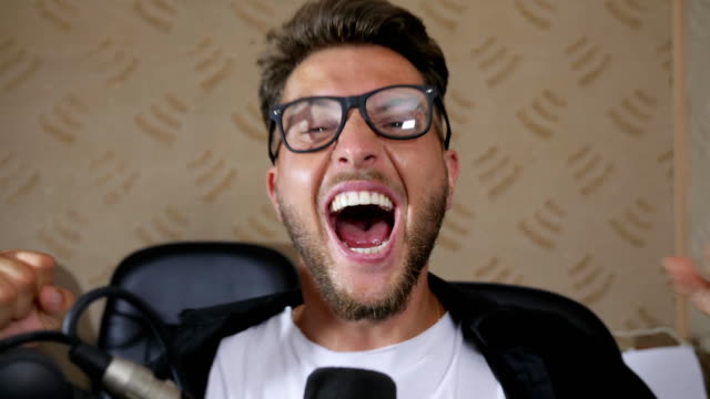 crazy-male-in-eyeglasses-with-wide-open-mouth-screams-into-microphone-indoors
