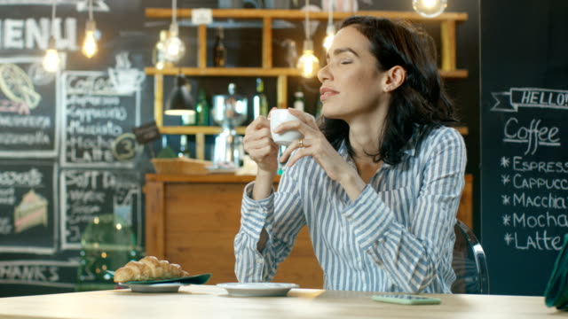 Schöne-Hispanic-Frau-entspannt-im-Café,-trinken-trinken-aus-der-Tasse,-Blicke-auf-ihr-Handy-wo-eingehende-Nachricht-zensiert.-In-den-Hintergrund-stilvolle-moderne-Coffee-House.