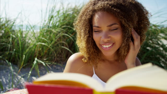 Portrait-of-voluptuous-Ethnic-female-reading-on-beach