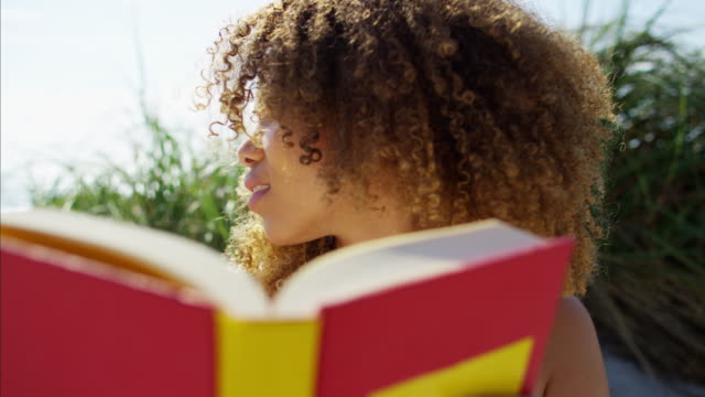 Afro-hair-Ethnic-female-reading-book-on-beach