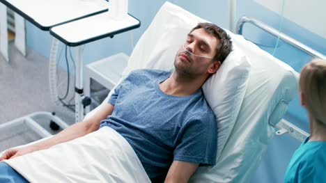 Im-Krankenhaus,-die-kranke-männliche-Patienten-auf-dem-Bett-schläft,-trägt-er-Nasenbrille.-Krankenschwester-betritt-und-prüft-seine-Tropfen-Zähler,-erhöht-die-Dosis-der-Schmerzmittel.