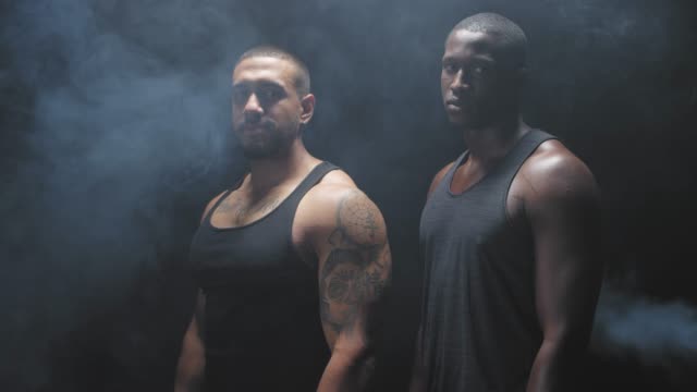 Portrait-shot-of-two-muscular-black-men-staring-at-the-camera-on-a-foggy-dark-background.