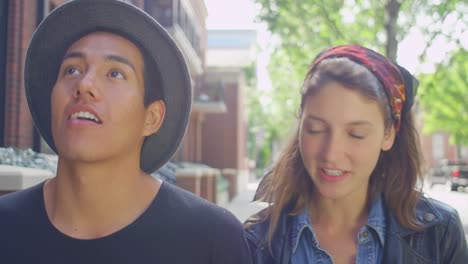 A-hipster-couple-walking-down-the-sidewalk-toward-the-camera,-talking-and-smiling