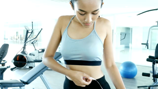 Asian-sport-girl-measuring-waist-with-white-ribbon.-Woman-exercise-at-fitness-gym.-Sport-and-Reaction-concept.-4k-Resolution.