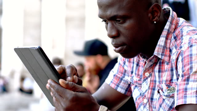 Retrato-de-hombre-negro-americano-joven-usando-la-tableta-digital---al-aire-libre
