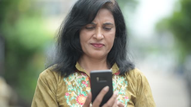 Madura-hermosa-mujer-India-con-teléfono-en-el-exterior-de-las-calles