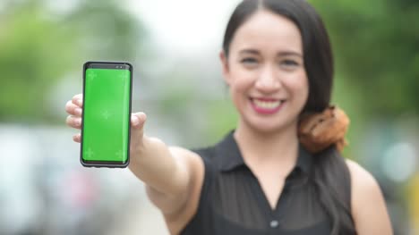 Junge-glücklich-schöne-asiatische-geschäftsfrau-zeigt-Telefon-in-der-Straßen-Natur