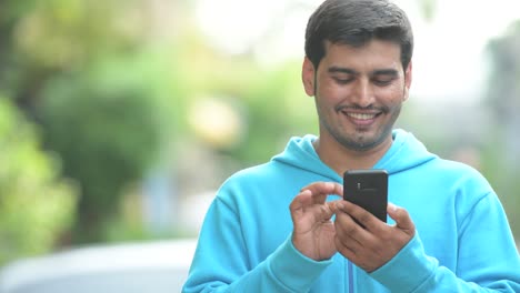 Young-happy-Persian-man-using-phone-outdoors