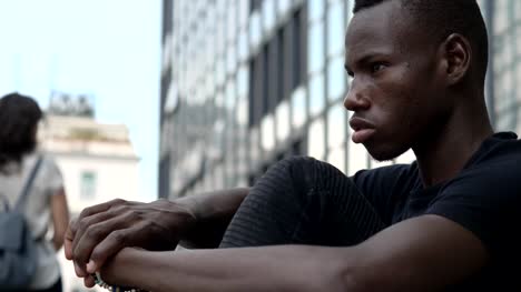 Nachdenklich-traurig-junger-afrikanischer-Mann-sitzt-in-der-Stadt
