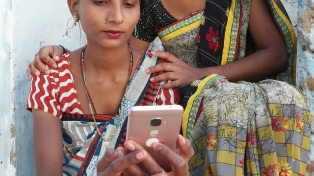 Neigen-Sie-zu-zwei-schönen-Frauen-in-traditionellen-Rajasthani-lokalen-Kleid-Kostüm-Sari-auf-dem-Handy-eine-Foto-Video-miteinander-teilen,-in-der-bequem-von-ihrer-Heimat-Gesicht-Porträt-süß-Hände-closeup