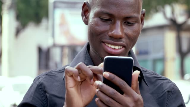 Sonriente-hombre-joven-africano-americano-utilizando-smarthone---al-aire-libre