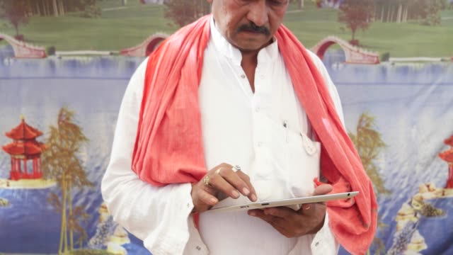Hombre-indio-mano-ocupada-en-una-tableta-de-pantalla-táctil-con-un-telón-de-fondo-de-la-tienda-muy-colorida