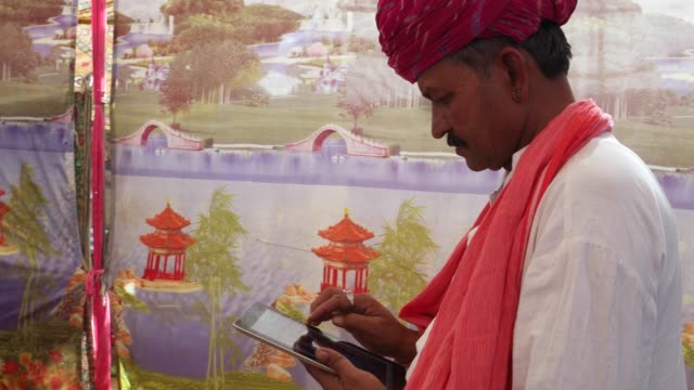 Handheld-indischer-Mann-damit-beschäftigt-auf-ein-Touchscreen-Tablet-mit-einer-wunderbar-bunten-Zelt-Kulisse