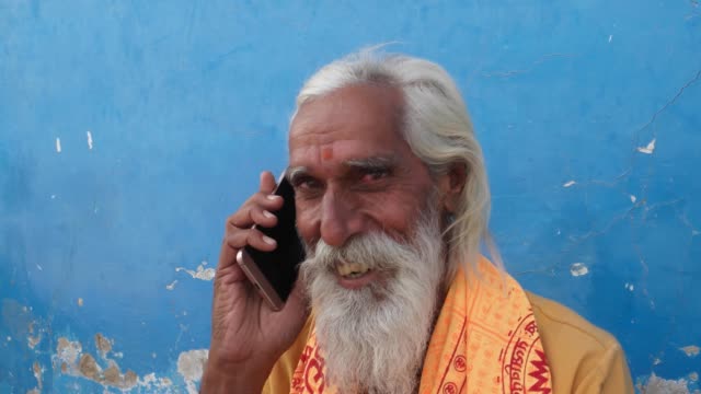 Handheld-Nahaufnahme-von-einem-Hindu-Sadhu-Lächeln-während-des-Besuchs-eines-Anrufs-auf-seinem-Handy