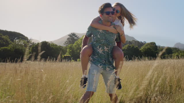 Piggyback-couple-laughing-in-long-grass-field-in-love