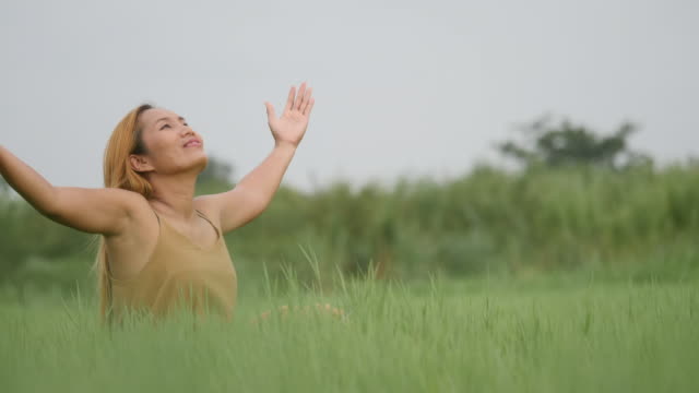 Joyful-Woman-Sitting-on-the-green-field-and-raising-her-hand-refresh-life