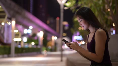 Beautiful-Asian-Woman-Outdoors-At-Night-Using-Mobile-Phone