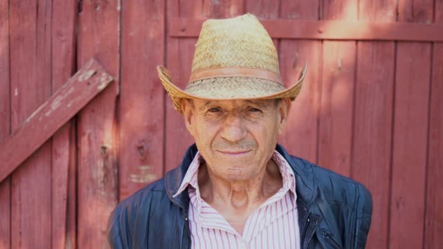 Portrait-of-an-elderly-farmer-in-a-straw-hat-on-a-farm-background.-Face-of-a-man-in-age