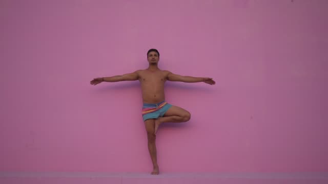 Mixed-race-hispanic-young-man-with-naked-torso-practicing-yoga-fitness-exercise-on-pink-background.-Sport,-meditation-and-lifestyle-concept.-Peaceful-Meditation-for-good-health