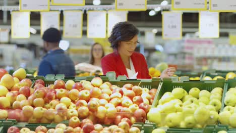 En-el-supermercado:-hermosa-mujer-Elige-frutas-orgánicas-en-el-fresco-producen-sección-del-mercado-del-agricultor.-Les-recoge-frutas-y-lugares-en-su-cesta-de-la-compra.-Cámara-lenta.