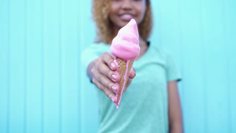 Chica-negra-feliz-muestra-rosa-helado-fusión-entonces-comienzo-a-comer-en-el-fondo-de-la-pared-azul