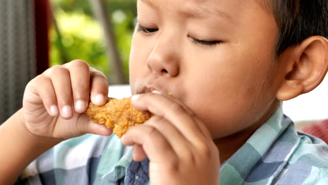 Cute-asian-boy-are-happy-eating-fried-chicken-leg-in-restaurant.-Video-4k-Slow-motion
