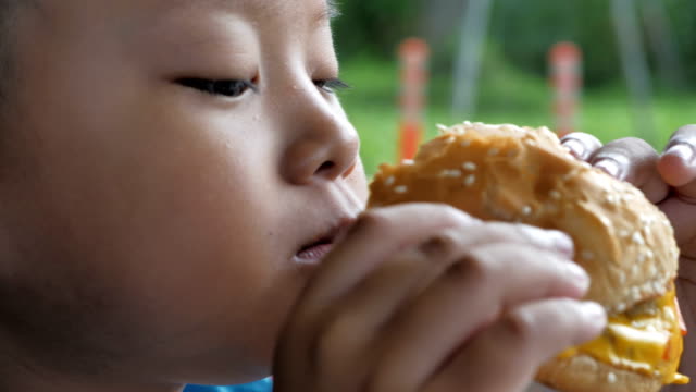 Close-up-little-asians-boy-enjoy-eating-burger,-Cute-happy-boy-holding-hamburger-at-restaurant.-video-Slow-motion