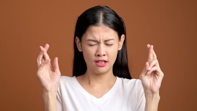 Chica-dedo-cruzado.-Mujer-asiática-joven-en-situación-de-camiseta-blanca-con-los-dedos-cruzados-para-la-buena-suerte-y-finalmente-gana-aislado-sobre-fondo-naranja.