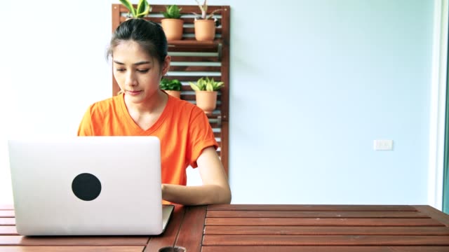 Mujer-usando-laptop-en-balcón-al-aire-libre.-Joven-mujer-sentada-en-el-balcón-utilizando-la-computadora-portátil-en-la-mesa-de-madera.-Concepto-de-nómada-digital.