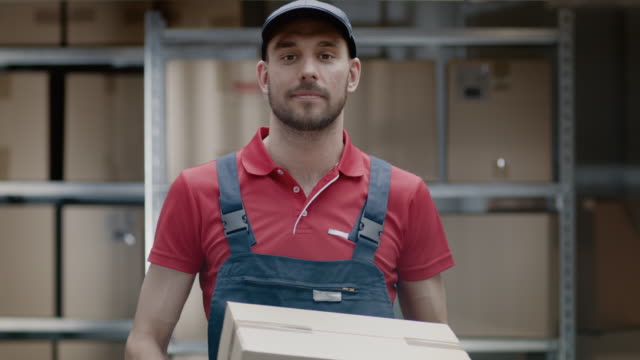 Portrait-der-schönen-Lagerarbeiter-in-Uniform-gibt-Karton-Verpackung-und-lächelt.