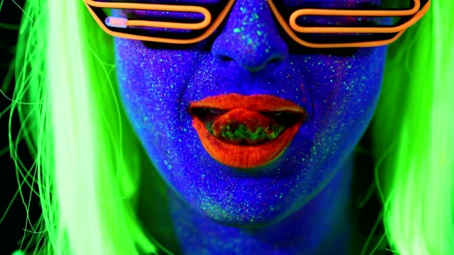Frau-mit-UV-Bemalung,-Perücke,-UV-Brille,-leuchtende-Kleidung-Porträt,-lecken-Lippen,-Gesicht-Nahaufnahme-oben-machen.-Kaukasische-Frau.-.