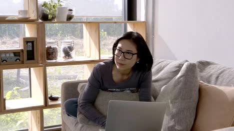 Schöne-Asiaten-junge-Frau-arbeiten-mit-Computer-Laptop-sitzend-auf-Sofa-zu-Hause.-Arbeit-zu-Hause-Konzept
