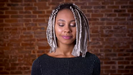 Young-African-girl-with-dreadlocks-arrogantly-looks-into-the-camera-and-smiles.-Brick-wall-in-the-background.