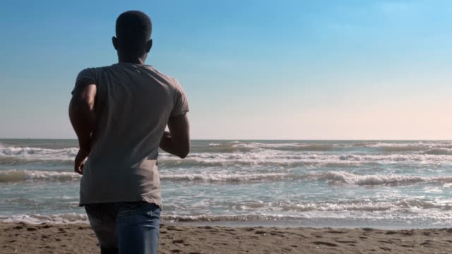 Laufen-Sie,-Natur,-Gesundheit.-junger-schwarzer-Mann-läuft-auf-den-Strand-Rückansicht