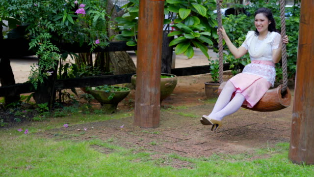 happy-young-woman-in-Thai-traditional-dress-relaxing-on-a-wooden-swing
