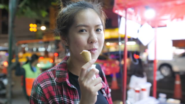 Young-attractive-asian-woman-enjoying-strawberry-ice-cream-in-waffle-cone-during-evening-at-night-market.