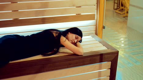 Beautiful-brunette-girl-is-lying-on-a-wooden-bench-in-a-sauna-behind-a-glass-door.-Girl-is-resting-with-her-eyes-closed.-Span-camera