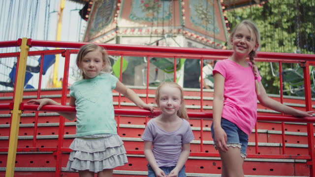 Drei-Mädchen-drehen-Sie-sich-um-und-Lächeln-vor-einer-Karneval-ride