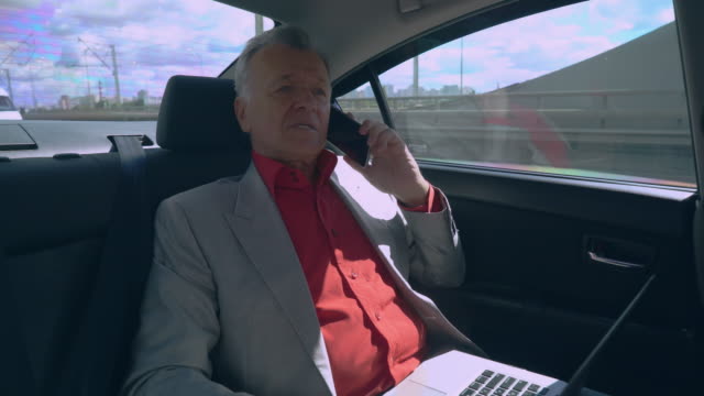 Businessman-using-mobile-phone-and-computer-in-car