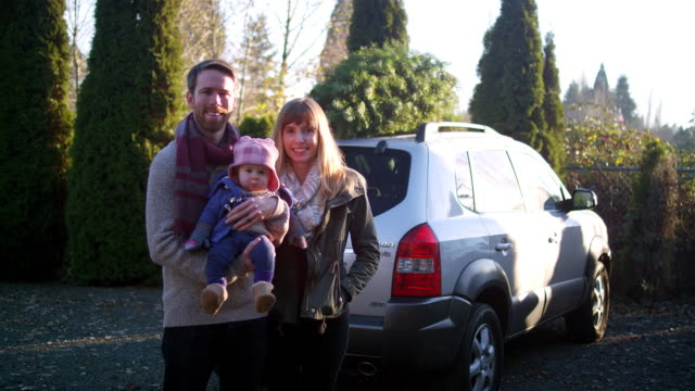 Portrait-of-a-young-mother,-father-and-baby-in-front-of-their-car-with-Christmas-tree-on-top