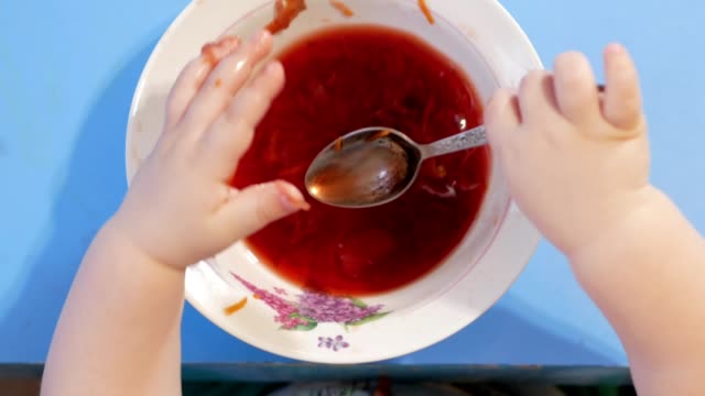 Eine-attraktive-junge-2-Jahre-alt-ist,-rote-Suppe-selbst-essen.-Er-klettert-seine-Hände-in-der-Platte.-Tabelle-Draufsicht