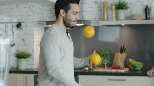 Lebhafter-junger-Mann-beeindruckt-seinen-Freundin-von-Jongling-Oranges-auf-der-Küche.