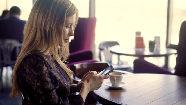 Young-pretty-female-using-phone.-Young-attractive-female-in-elegant-dress-sitting-at-table-with-coffee-and-using-smartphone